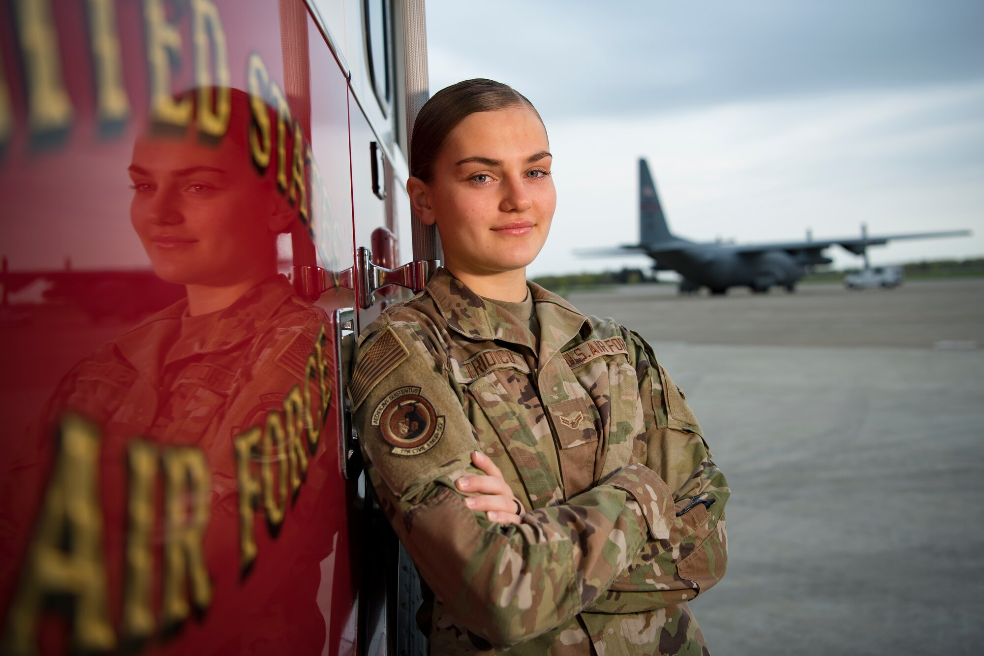 Airman stands by fire truck on flight line with C-130H Hercules