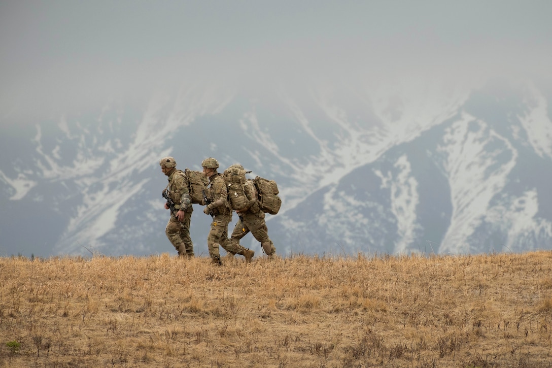 Three soldiers walk together with mountains in the background.