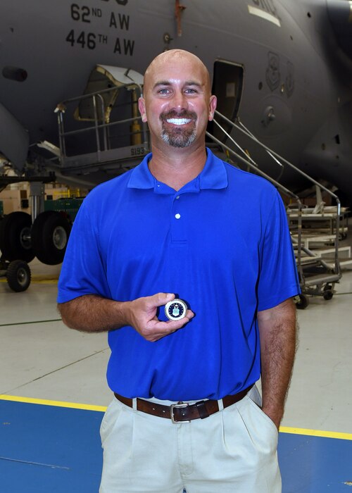 Photo shows a man holding a coin in front of an aircraft