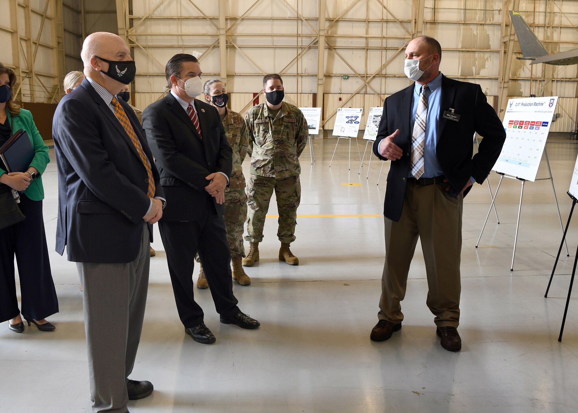 Photo shows group of people standing around boards on easels in front of an aircraft.