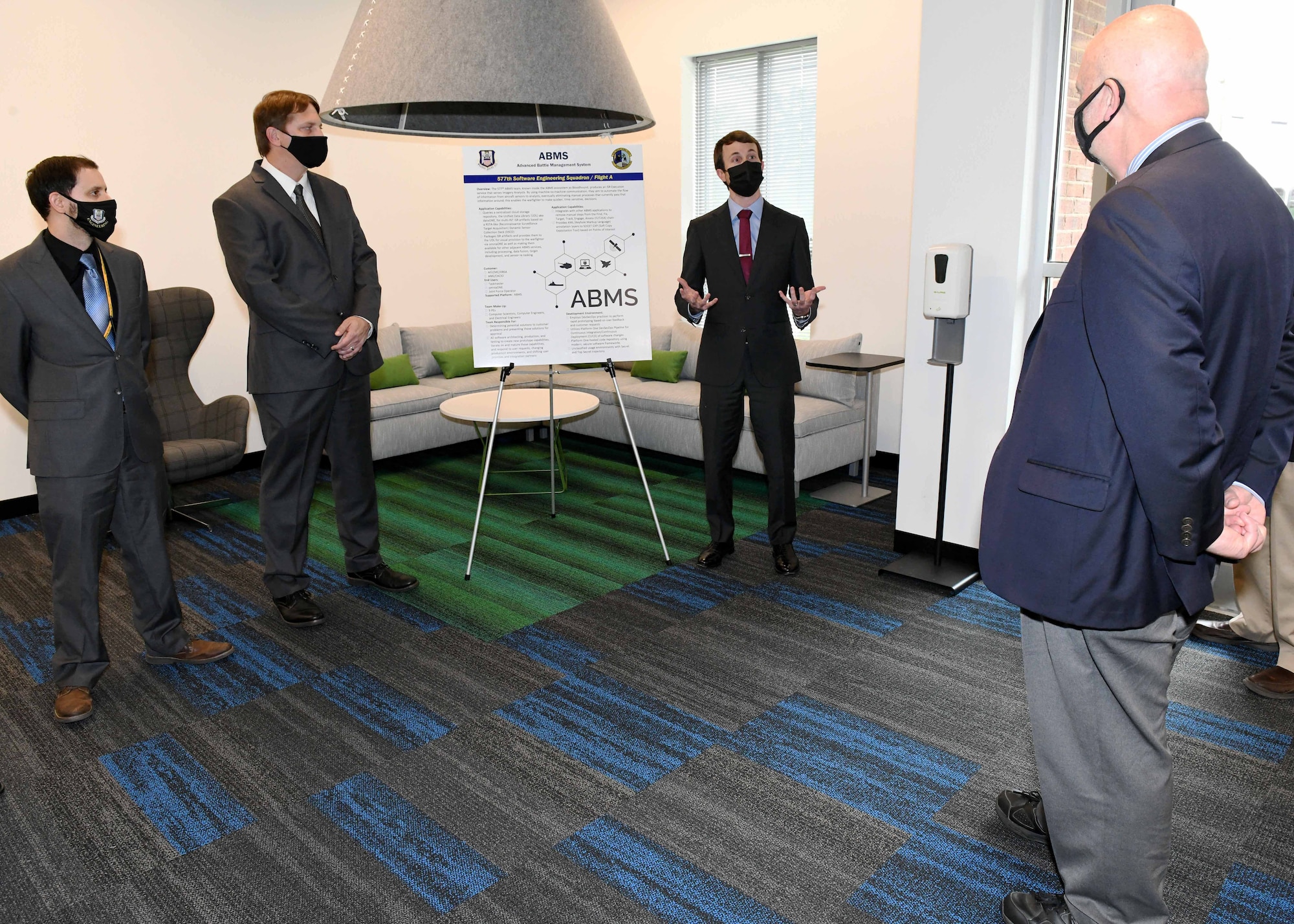 Photo shows group standing in room looking at a board on an easel.