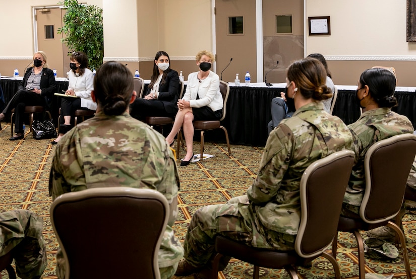 Military and civilian women sit facing one another in a large room.