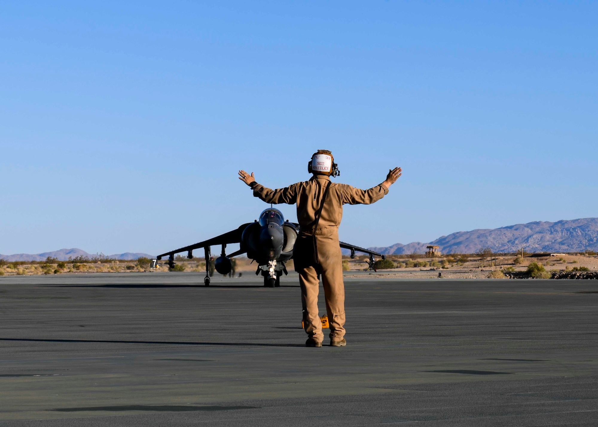 A U.S. Marine assigned to the Marine Corps Air Ground Combat Center directs a Harrier Jump Jet to a spot on the airfield for hot pit refueling at Marine Corps Air Ground Combat Center, California, May 4, 2021. This large-scale exercise prepared Marines for their upcoming deployments. (U.S. Air Force photo by Airman 1st Class Kiaundra Miller)