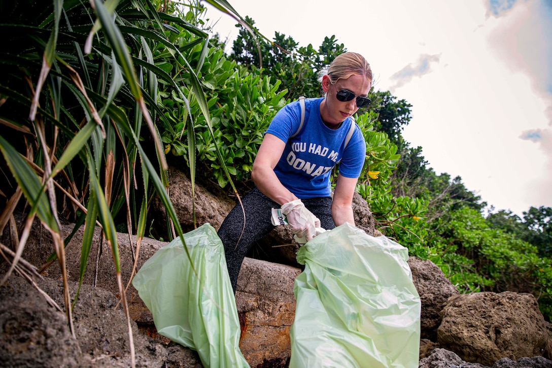 A Marine picks up in the trash in the woods.