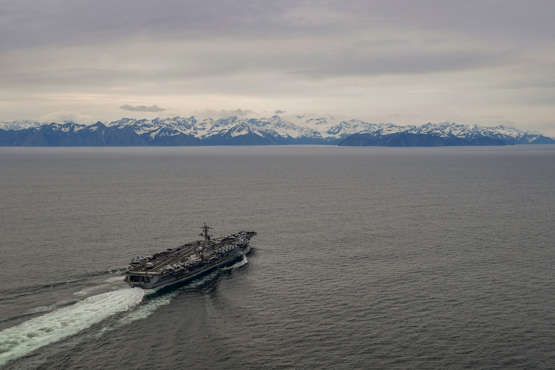 A ships transits a body of water with snowy mountains in the background.