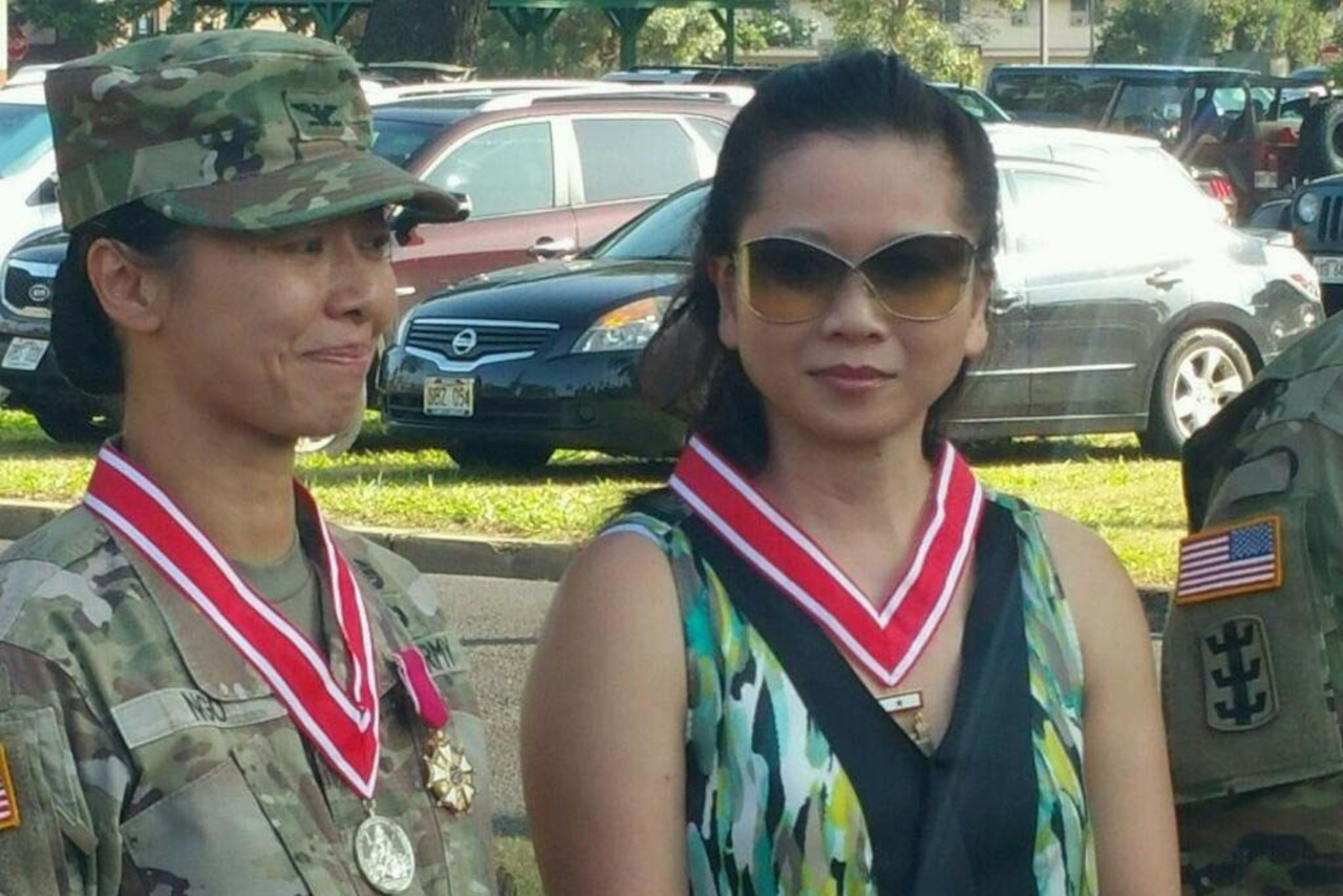 Two women, one in a military uniform, stand next to each other. Each is wearing an award on a ribbon.