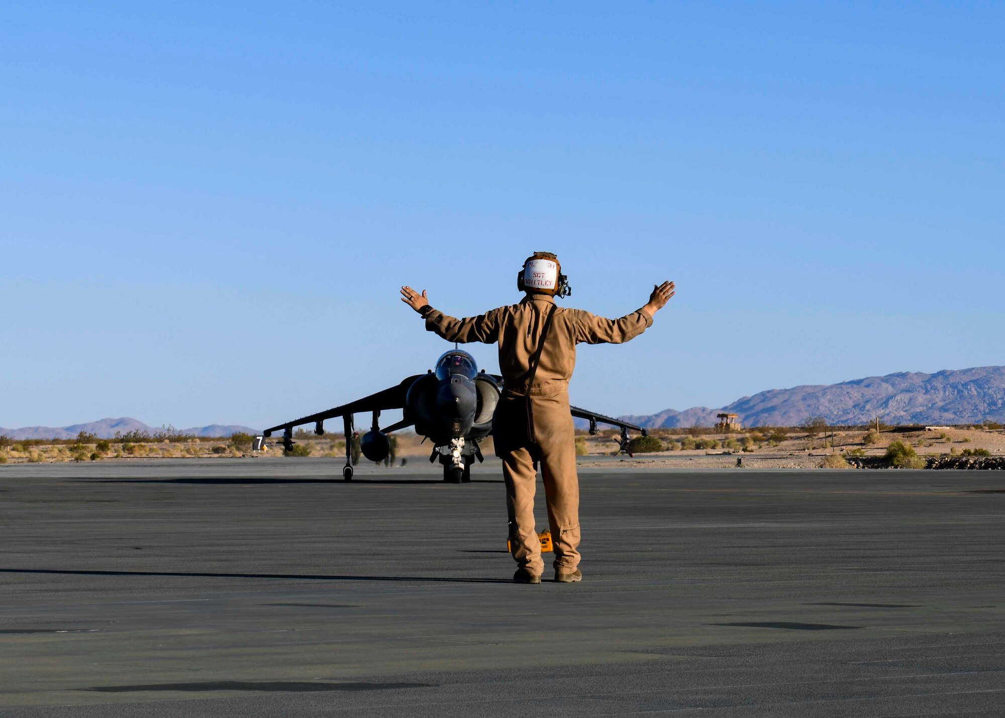 A U.S. Marine assigned to the Marine Corps Air Ground Combat Center directs a Harrier Jump Jet to a spot on the airfield for hot pit refueling at Marine Corps Air Ground Combat Center, California, May 4, 2021. This large-scale exercise prepared Marines for their upcoming deployments. (U.S. Air Force photo by Airman 1st Class Kiaundra Miller)