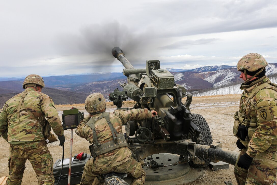 Three soldiers work together to fire a howitzer.