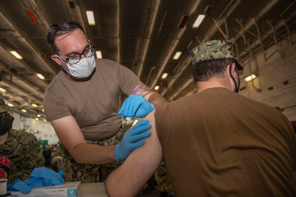 Hospital Corpsman 2nd Class Dillon Dixon, from Cleburne, Texas, assigned to USS Gerald R. Ford’s (CVN 78) medical department, administers a COVID-19 vaccine.