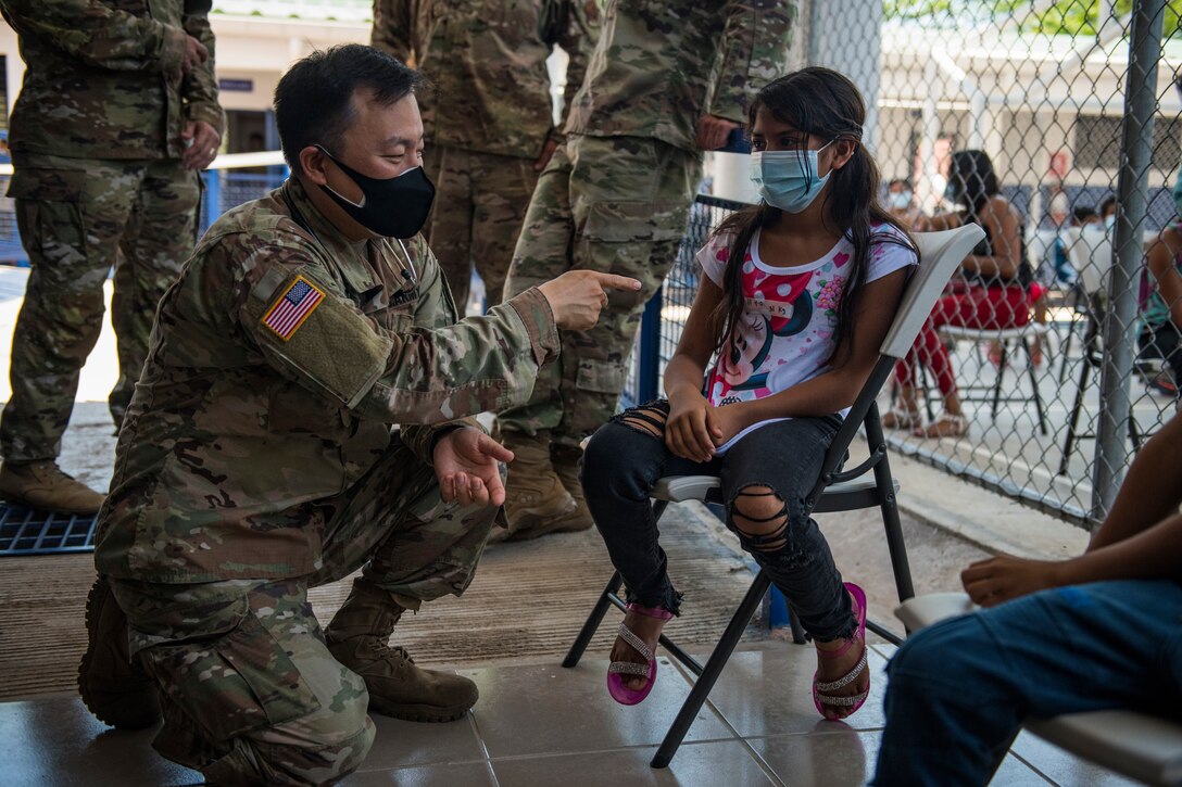 A soldier kneels as he speaks to a young woman sitting in a chair.