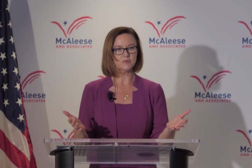 A woman standing at a lectern speaks.