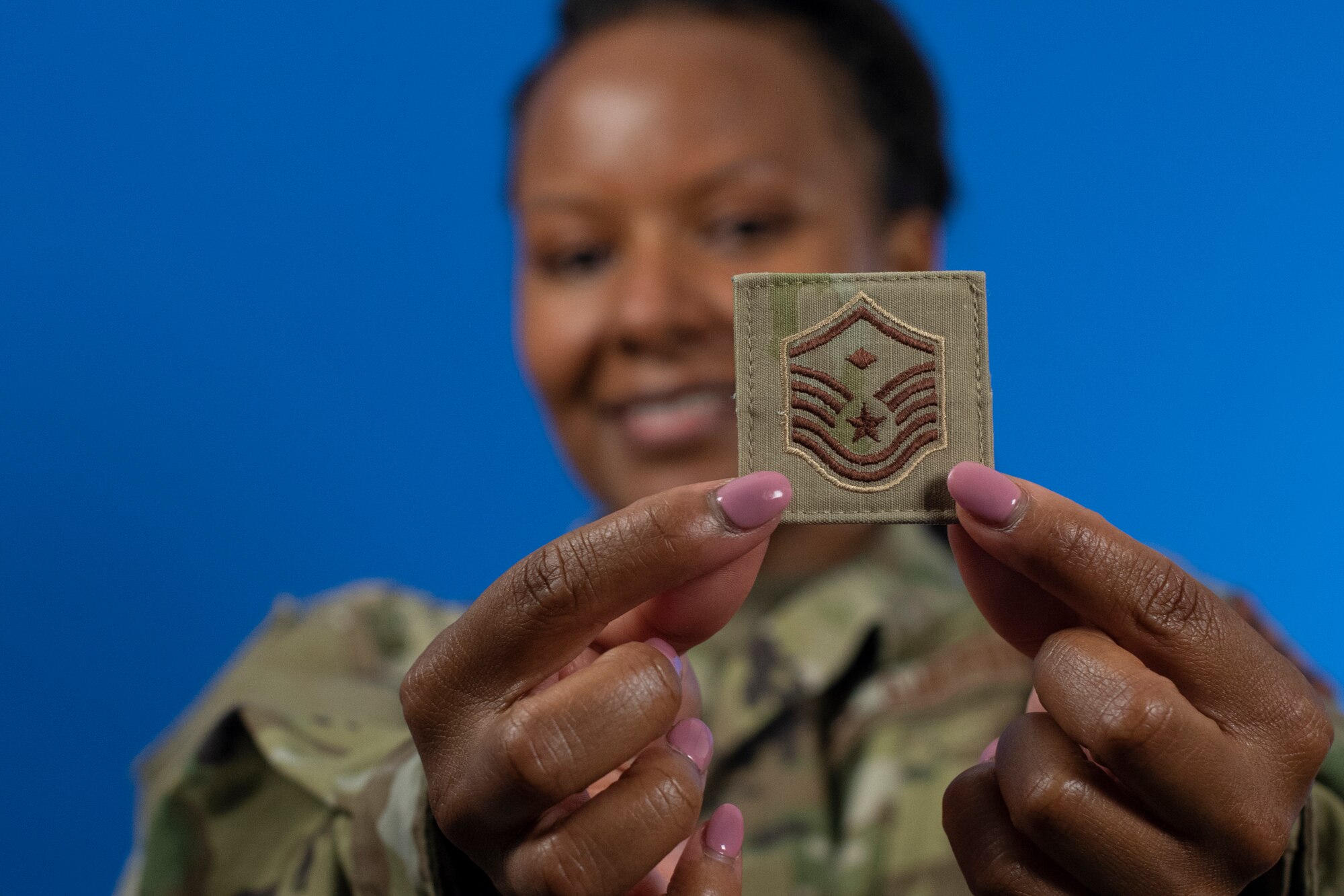A woman in an Air Force uniform holds up a patch with the first sergeant rank.