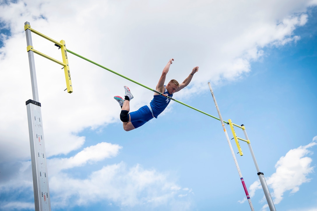 An Air Force cadet flies through the air with arms stretched upward toward a parallel bar.