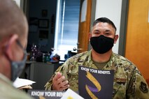 Airman speaks to another Airman while holding a book.