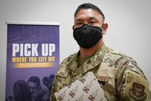 Airman holds binder standing in front of banner.