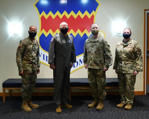 Four individuals pose in front of the 55th Wing emblem.