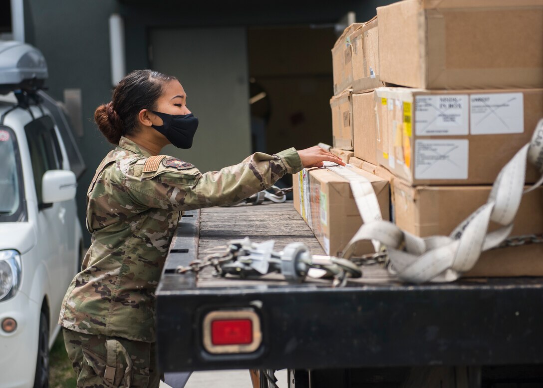 Woman in uniform inspects boxes on a truck bed.