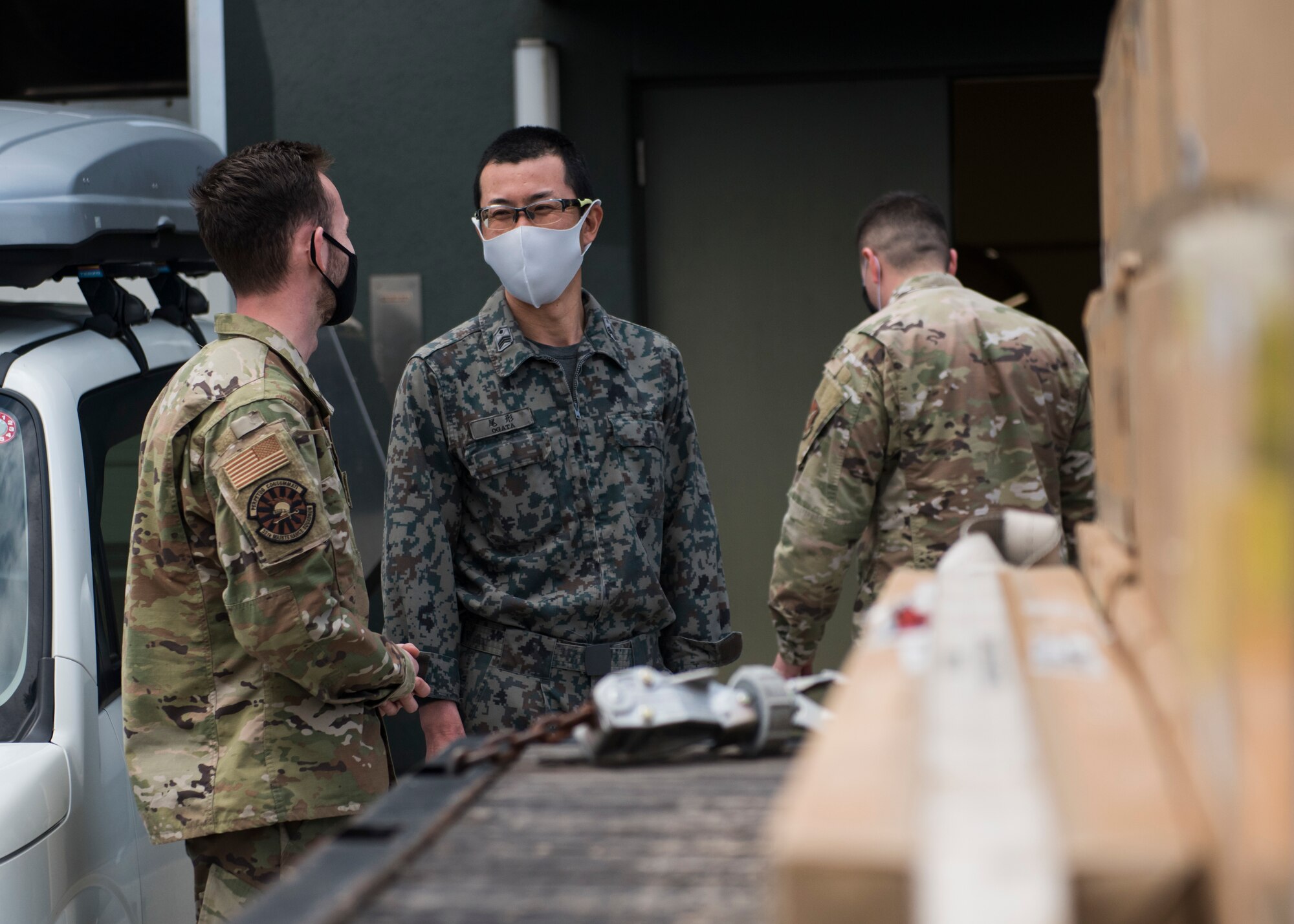 Men in U.S. and Japanese military uniforms talk next to F-35 egress parts.