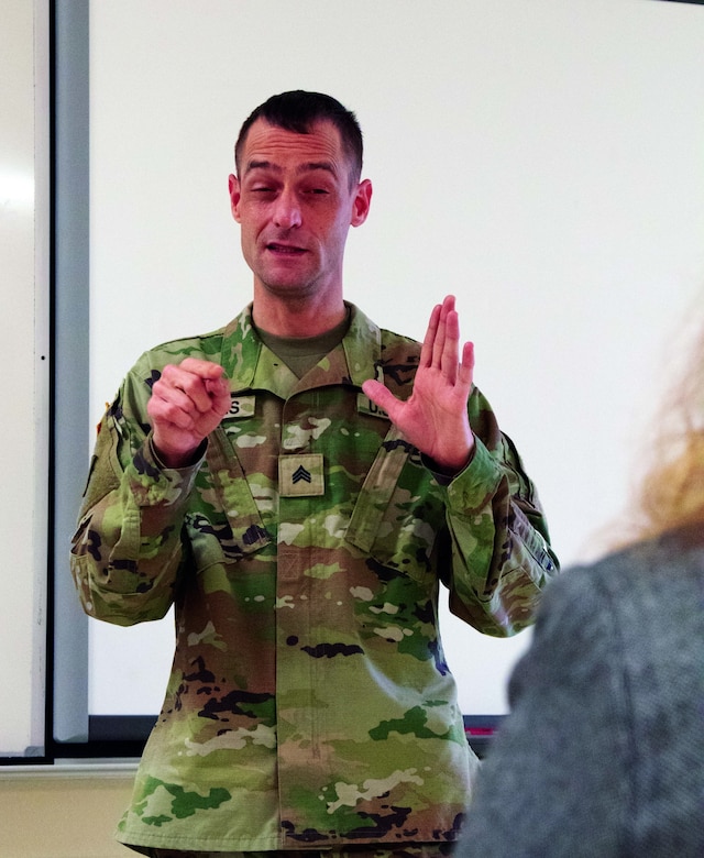 Michigan Army National Guard Sgt. Bill Fitrakis, 1460th Transportation Company, certified in American Sign Language, explains the COVID-19 vaccine process during a vaccination clinic at the Marine City Middle School in Marine City, Michigan, April 27, 2021. Due to most of sign language being a visual language, he cannot wear a mask as it would not impart the message.