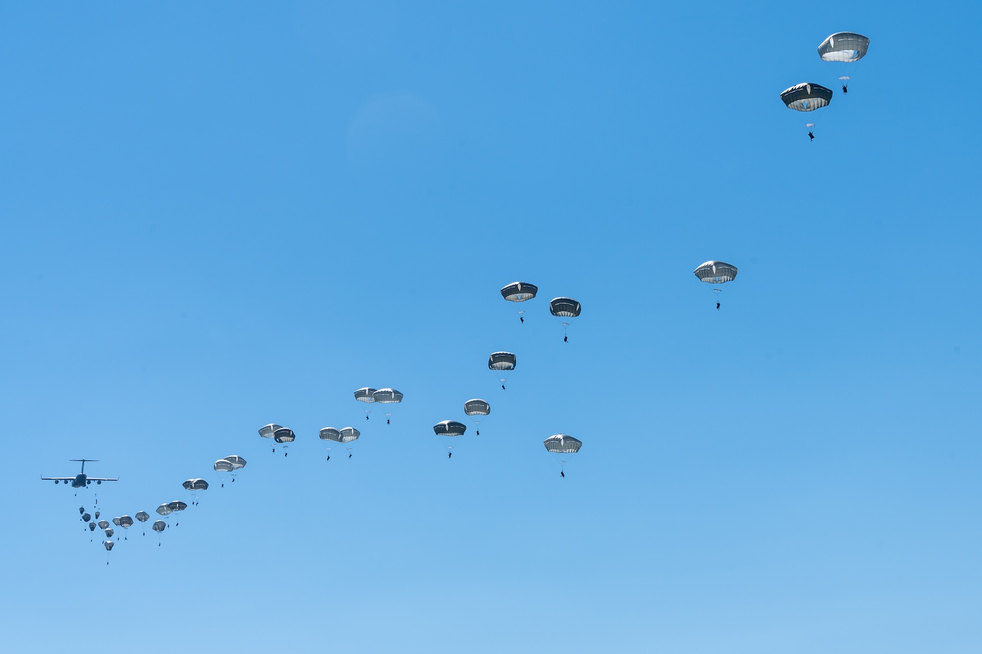 A trail of paratroopers behind an aircraft.