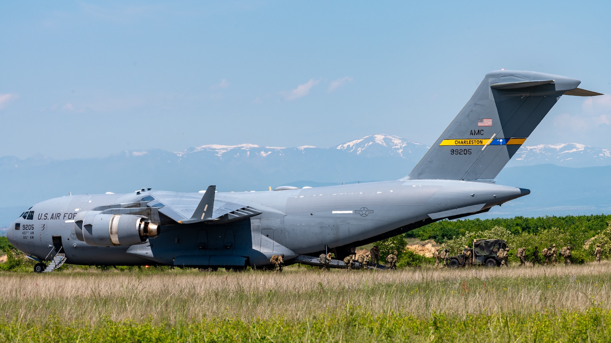 A aircraft sits on an airfield, while Airmen and Soldiers unload cargo.