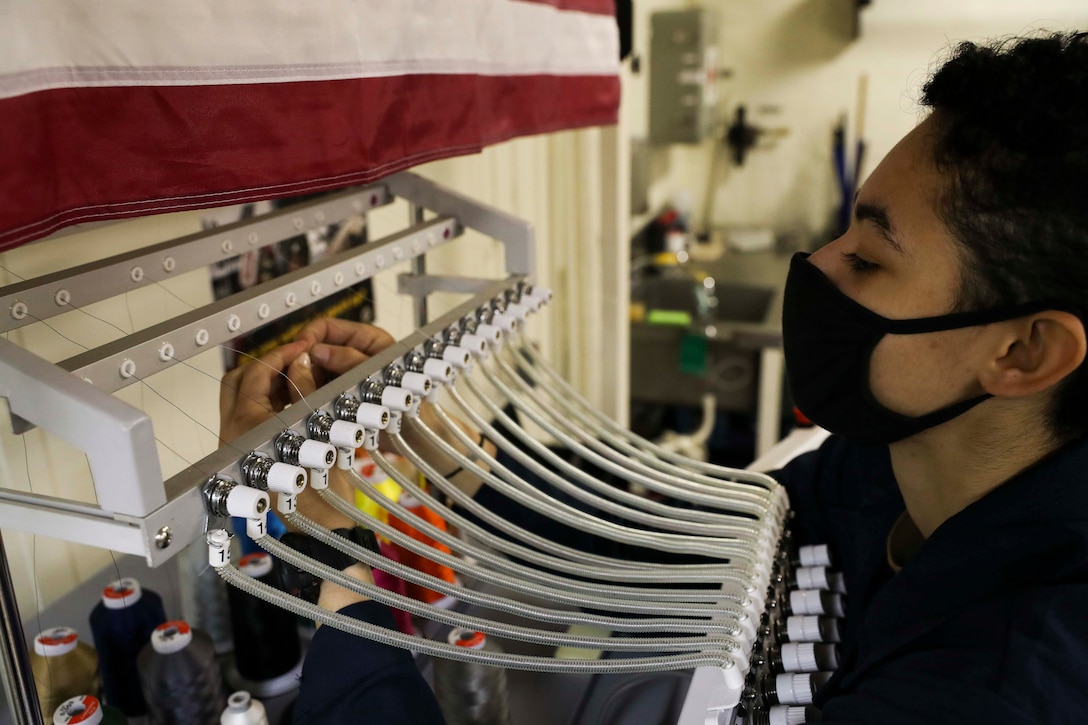 A sailor wearing a facemask puts thread in a sewing machine.