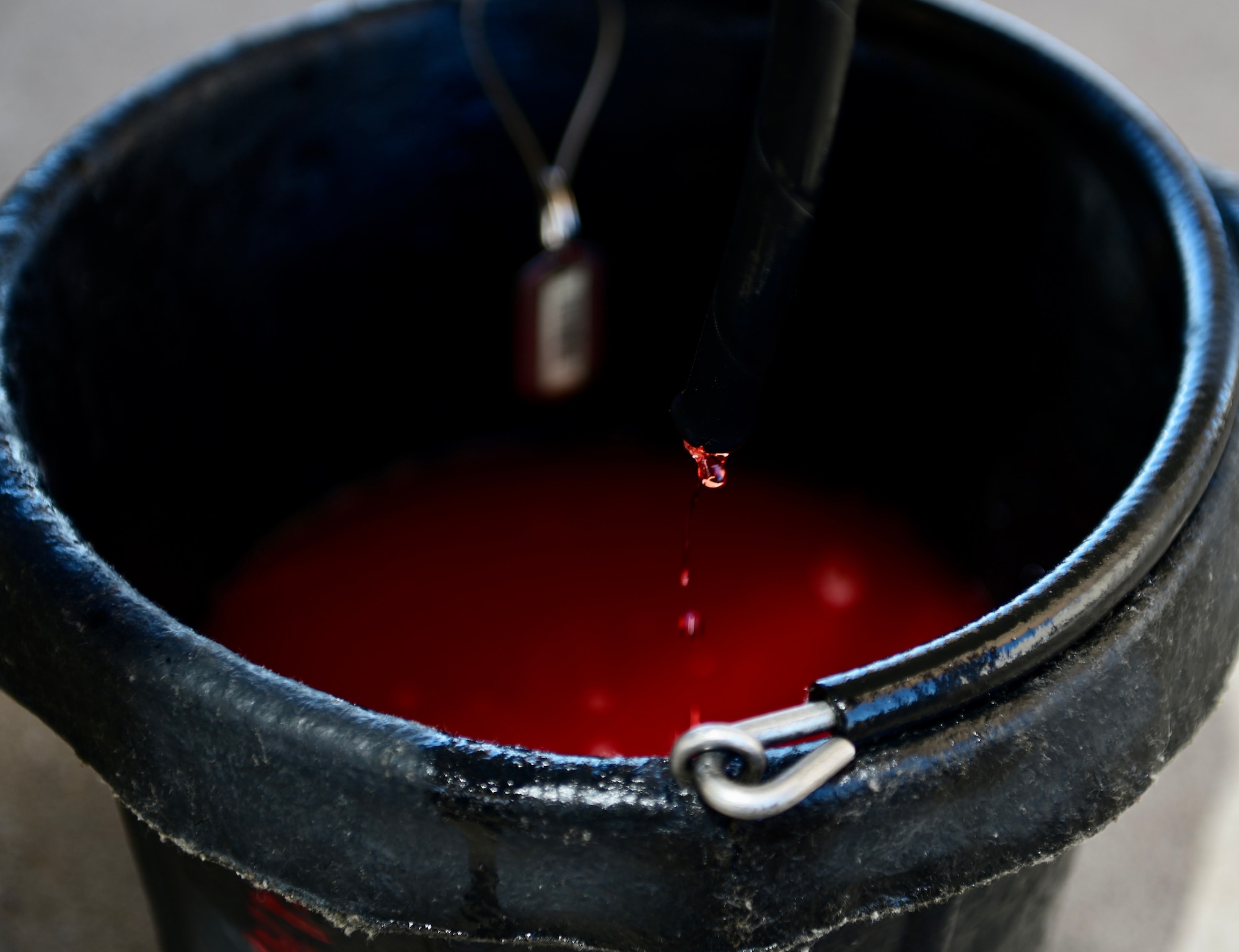 photo of a bucket on the ground with a small hose above it dripping red hydraulics fluid