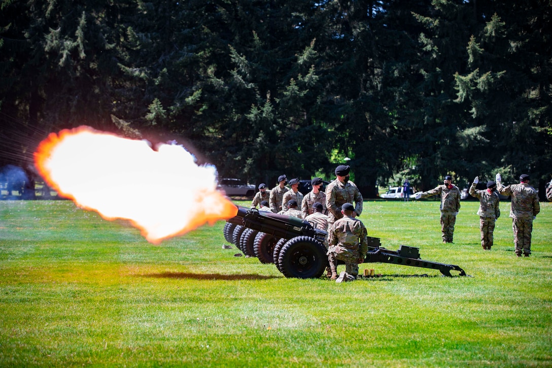 Soldiers fire a row of cannons on a field.