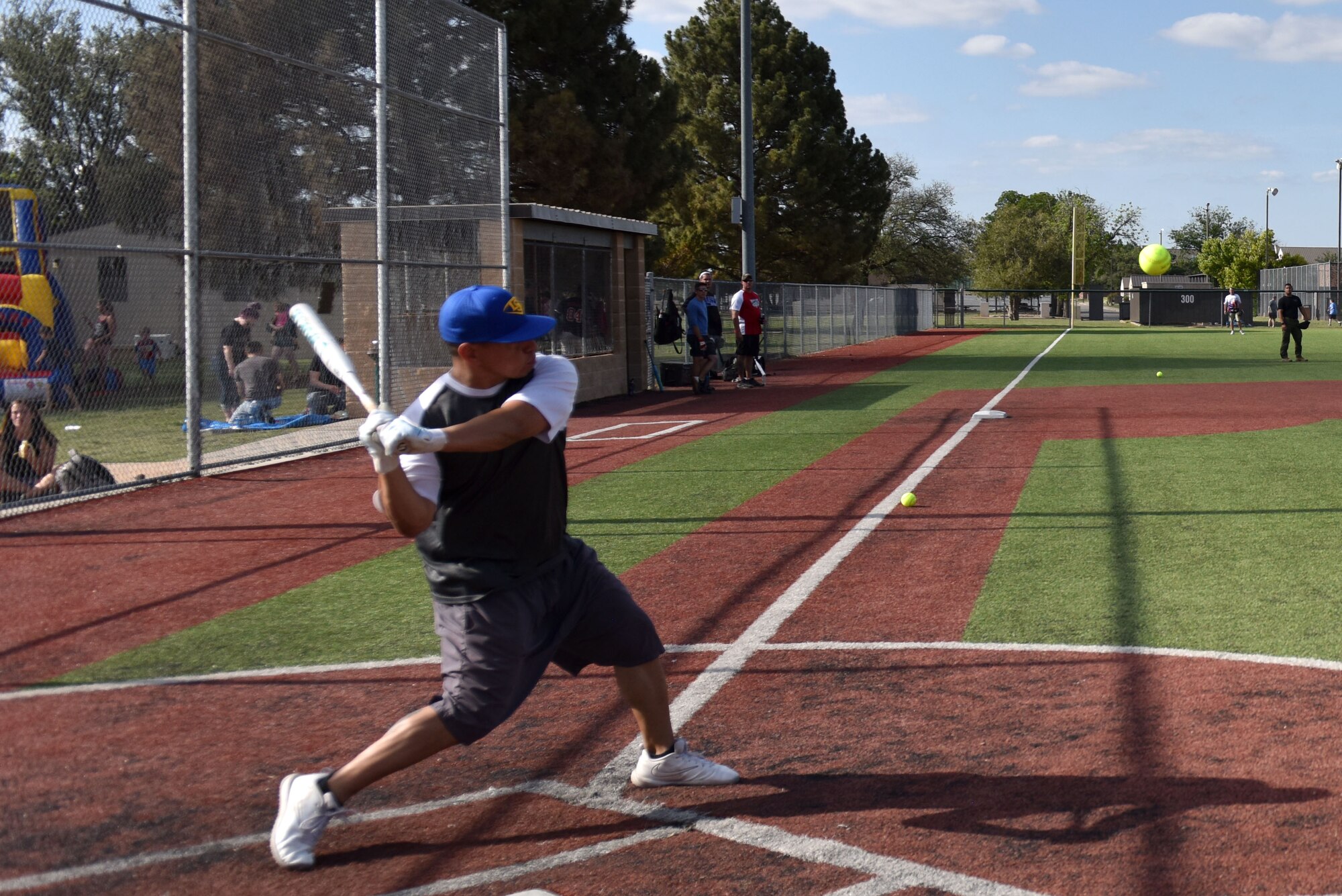 Individual swinging a bat towards a softball on a softball field.