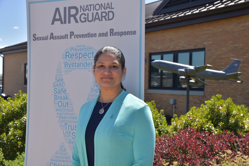 An airman poses for a photo next to a poster.