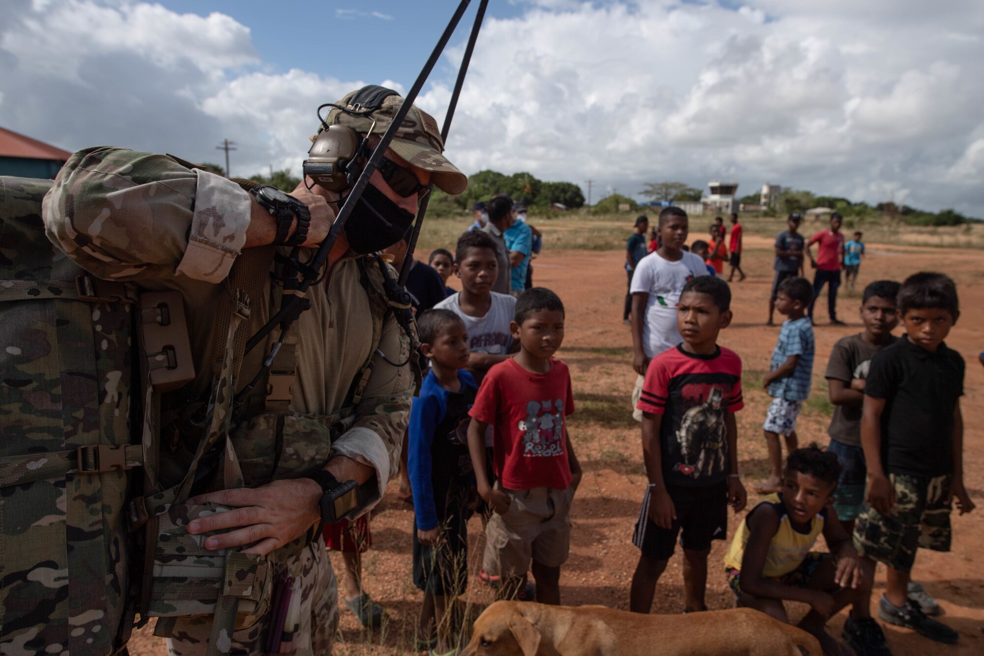 A U.S. Air Force Special Tactics operator carries equipment across the airfield while Honduran locals wait for hurricane relief supplies at Puerto Lempira, Honduras,