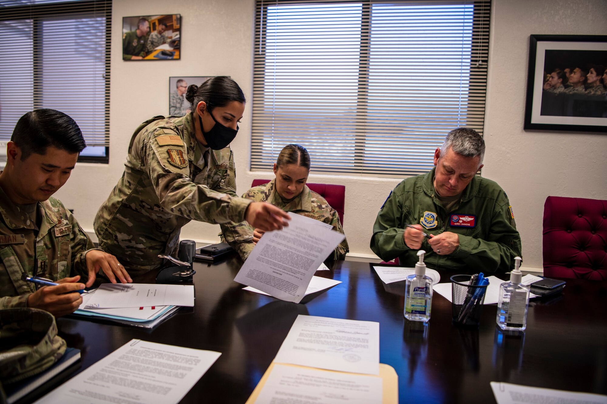 Four Airmen are huddled around a table signing paperwork.