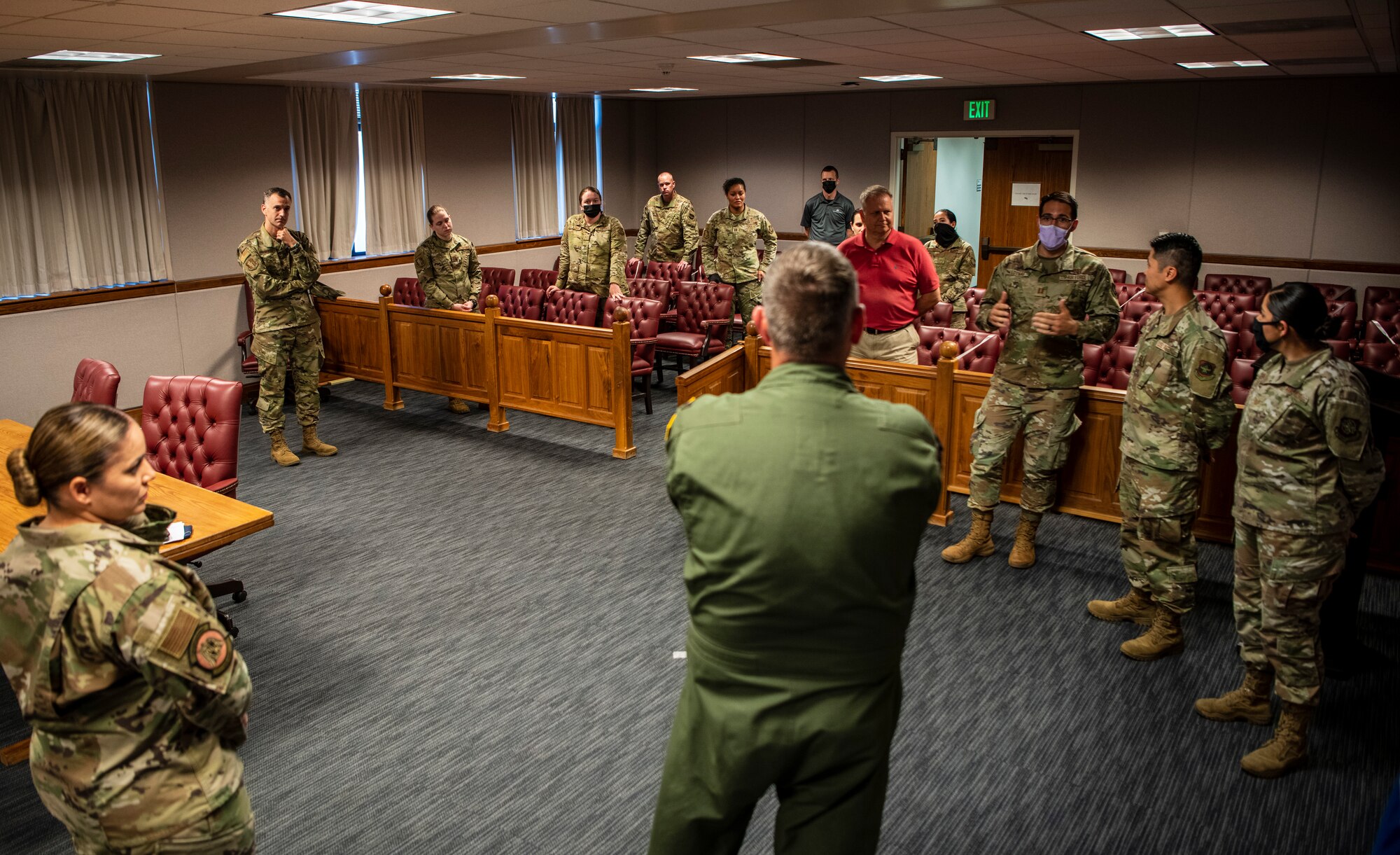 A group of people are in a courtroom listening to an Airmen brief leadership from the base.