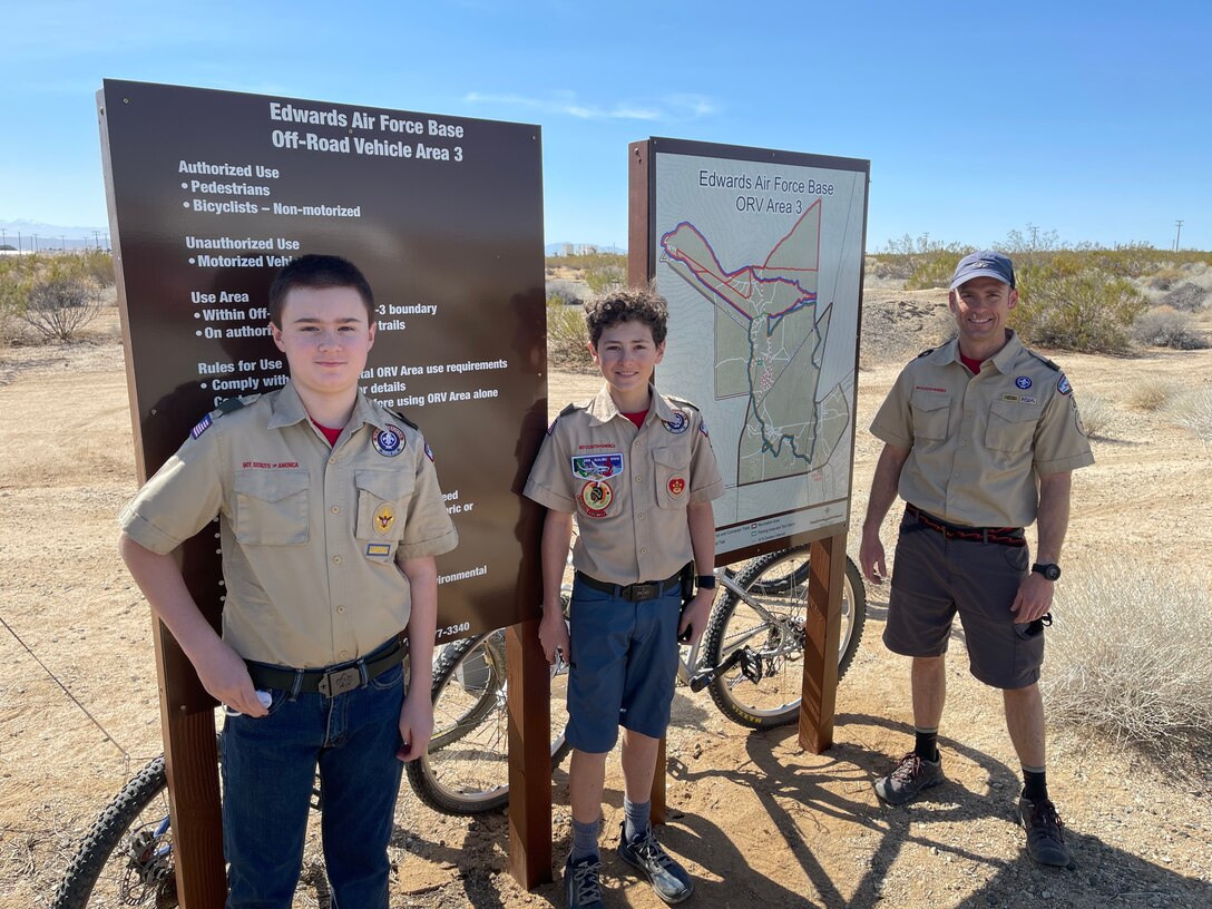 Lt. Col. Scott Fann, right, deputy commandant, U.S. Air Force Test Pilot School, along with son William Fann, center, and Allan Scott pose next to the new map and sign of the newly marked off-road trail at one of the trail heads on Edwards Air Force Base, California, during the grand opening, March 6.