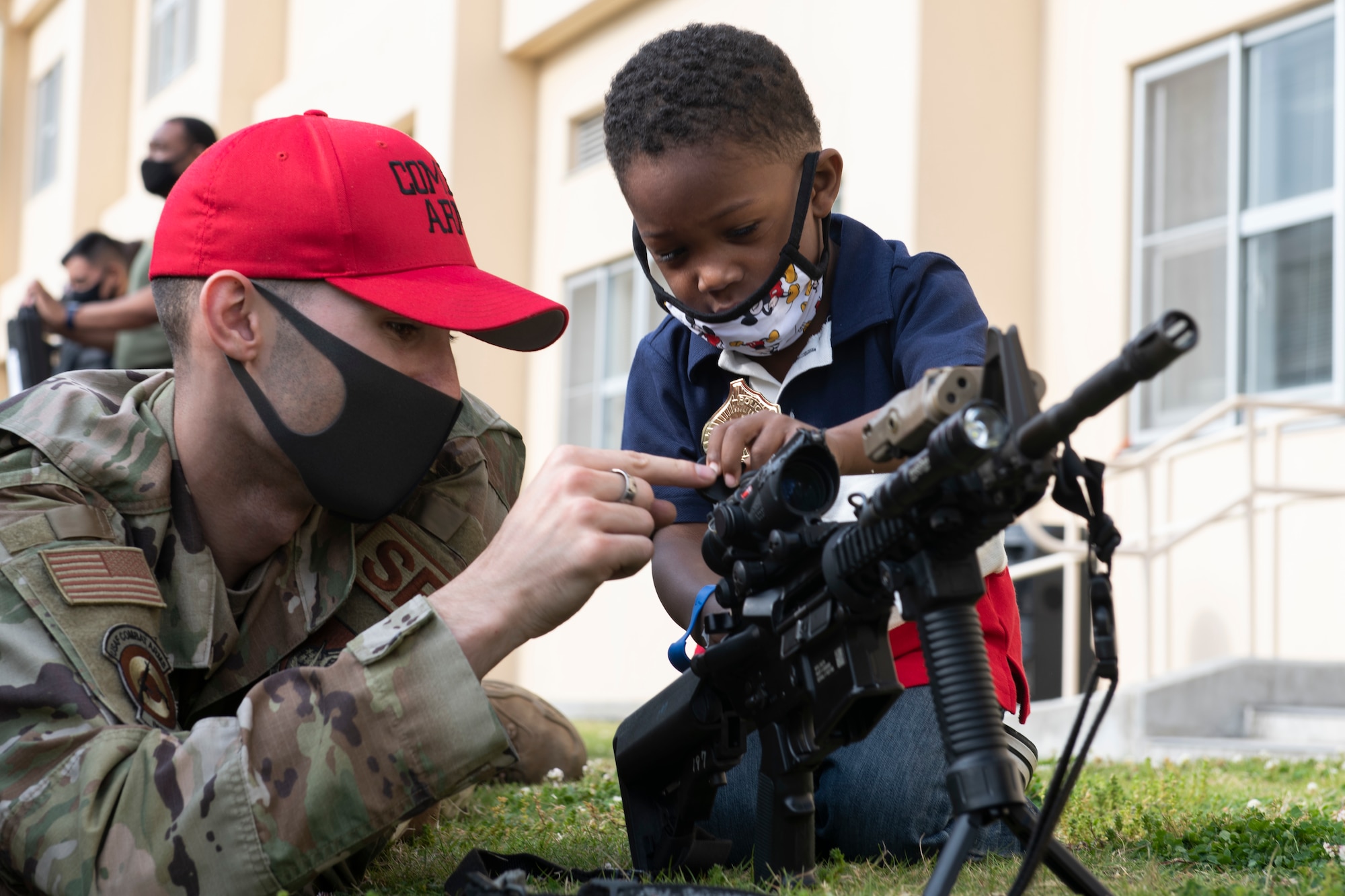 Staff Sgt. Boaz Rogel, 374th Security Forces Squadron Combat Arms instructor, left, teaches Khyran Grandison how a scope works at the “Day in the Life” event during National Police Week at Yokota Air Base, Japan, May 11, 2021.  The event featured booths from combat arms and military working dogs as well as the Air Force Office of Special Investigations to help familiarize the base on they protect the base. (U.S. Air Force photo by Staff Sgt. Joshua Edwards)