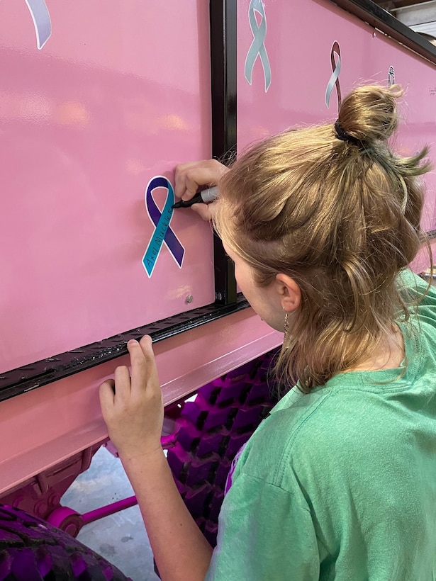 Girl in green shirt signs an awareness ribbon on a pink truck