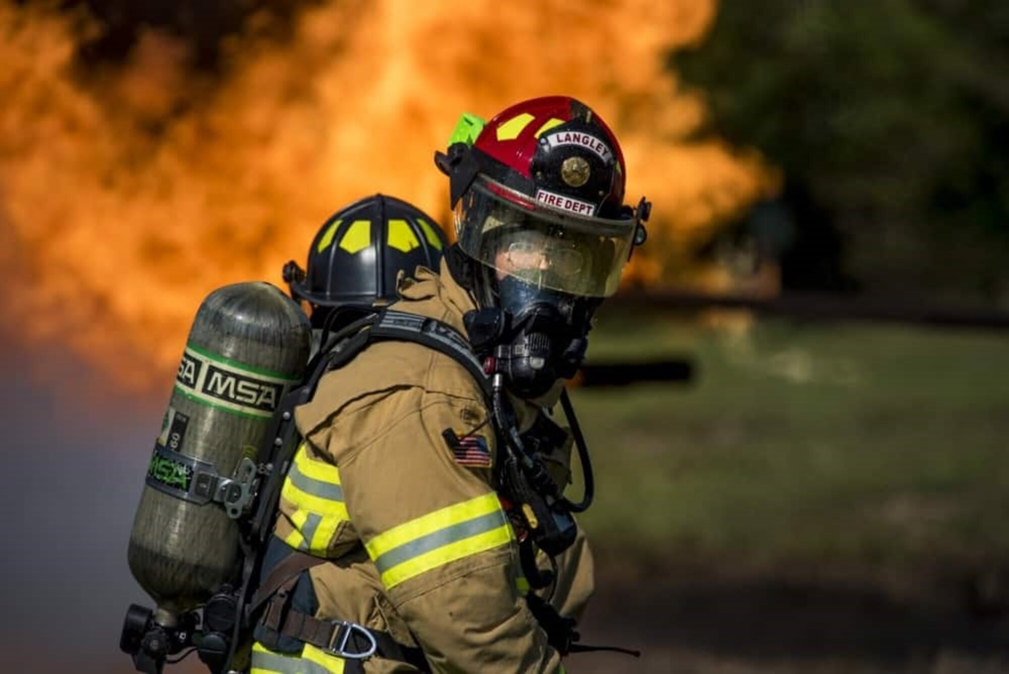 a photo of a fire fighter with his helmet and mask on in-front of a fire
