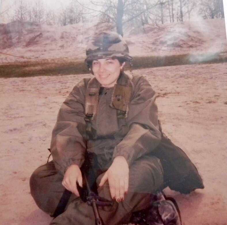 A woman wearing military fatigues and holding an M16 rifle poses for a photo.