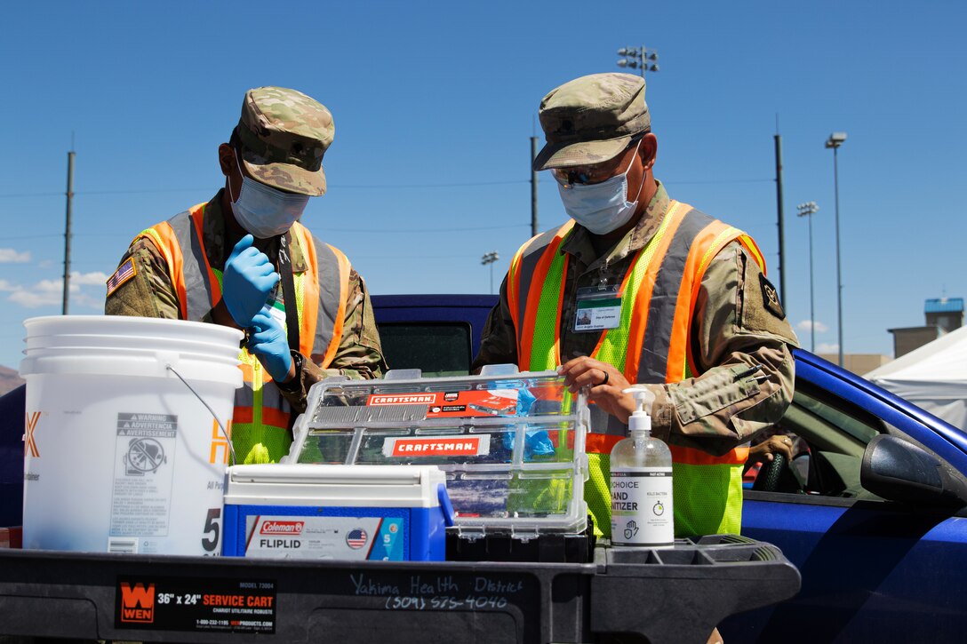 Two soldiers one wearing a face mask and gloves and the other only wearing a face mask prepare vaccinations at a community vaccination center.