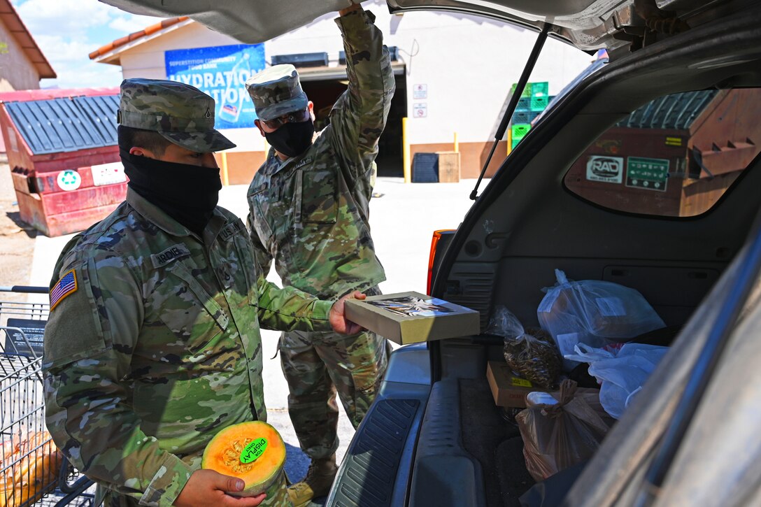 Arizona National Guard Guardsmen wearing face masks place groceries into the trunk of a car during a community food bank.