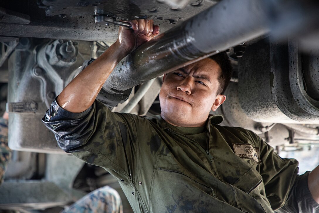 A Marine grimaces as he turns a wrench while working under a vehicle.