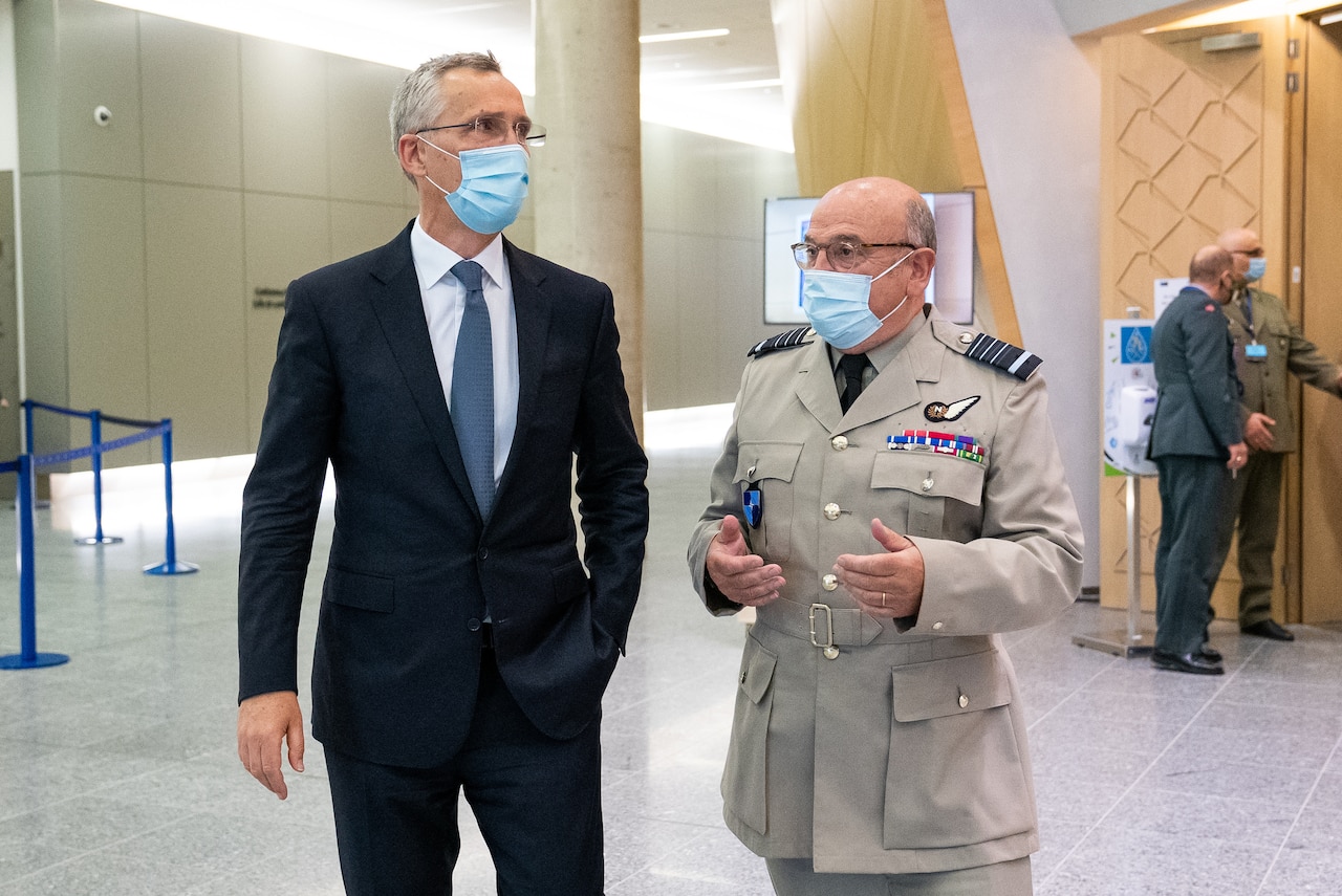 Two men wearing face masks speak.