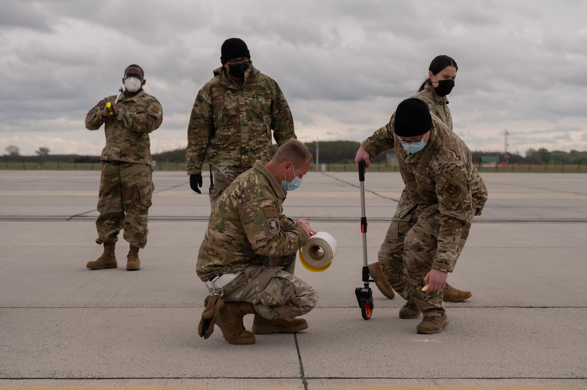 A group of Airmen standing and kneeling to mark spots on an airfield.