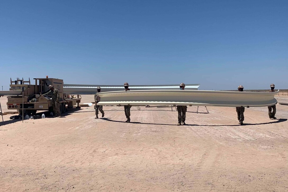 A group of men carry a long and large piece of metal.