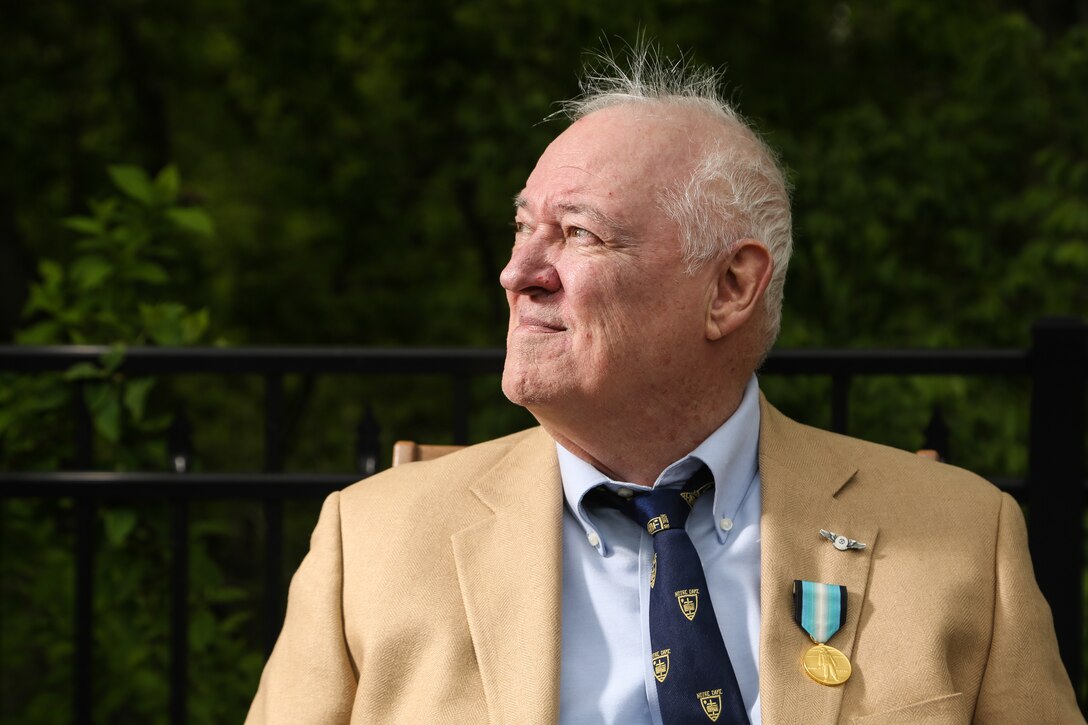 A man in a suit jacket wearing a medal pin looks to his right.