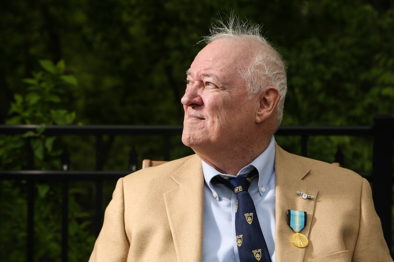 A man in a suit jacket wearing a medal pin looks to his right.