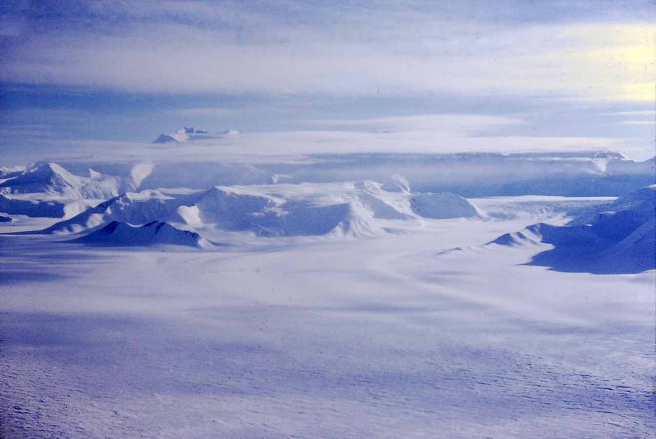 An aerial view of land shows vast snow-covered plains and mountains.