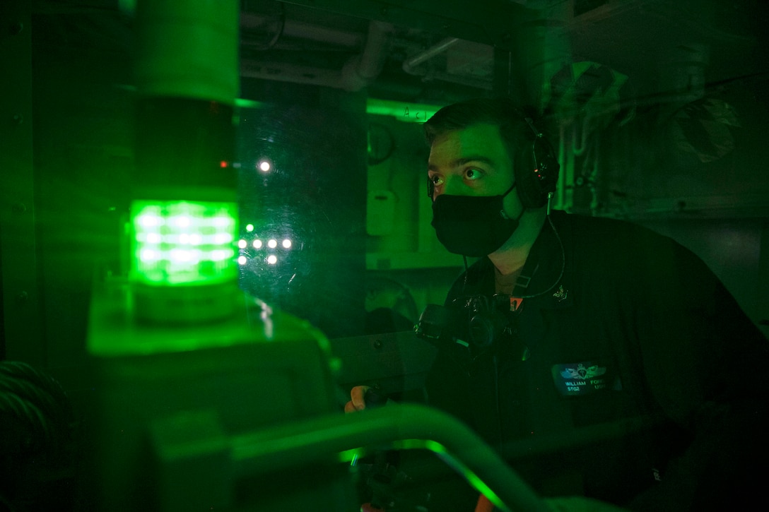 A sailor monitors a board aboard a ship bathed in green light.