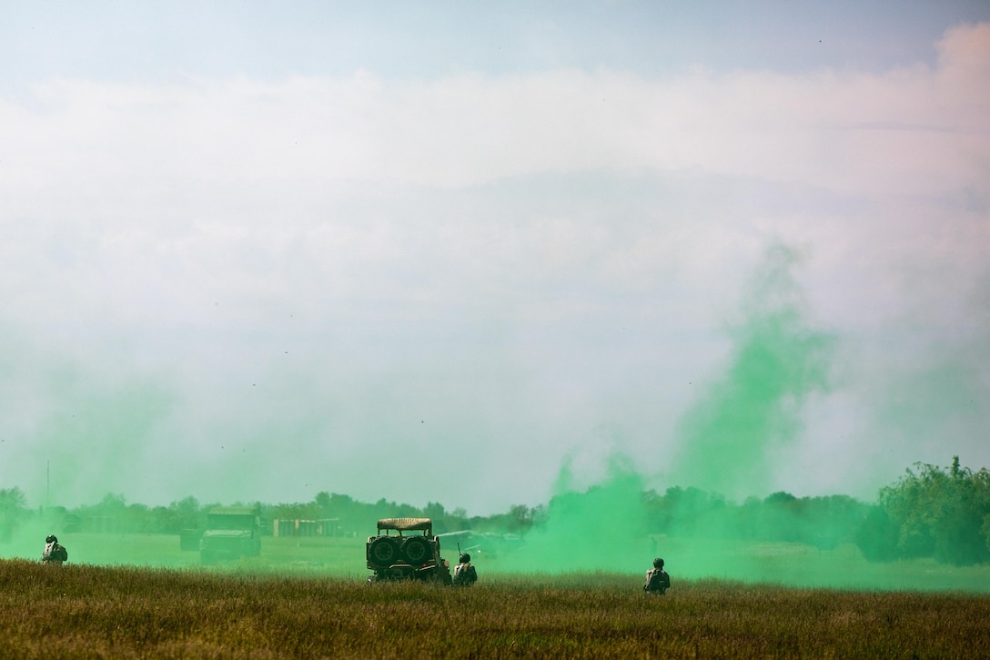 Troops train using green smoke in a field.