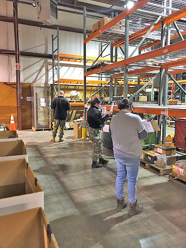Two military members and a civilian look for items in a warehouse.